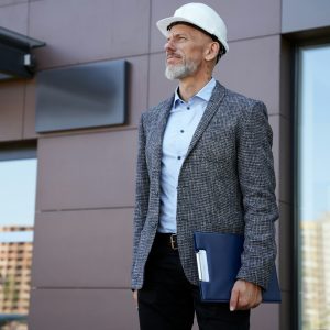 Monitoring the progress. Focused middle aged architect, engineer manager wearing helmet looking Monitoring the progress. Focused middle aged architect, engineer manager wearing helmet looking